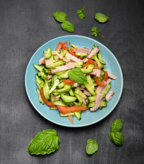 cucumber and ham salad next to Basil leaves and pepper on a white