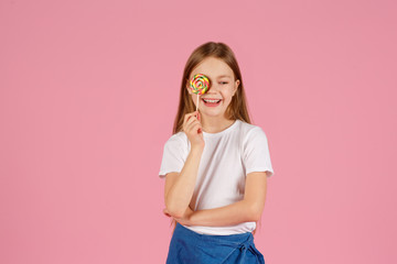 Portrait of a surprised little girl holding heart shaped lollipop and looking at camera isolated over pink background.