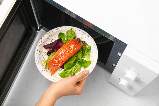 Woman putting plate with food in microwave oven