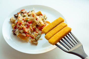 frying fish sticks in a pan. Homemade breakfast. Rice with vegetables and fried fish sticks.
