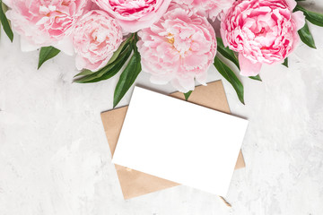 Blank greeting card and envelope with pink peony flowers on concrete background. Wedding invitation. Flat lay. Mock up