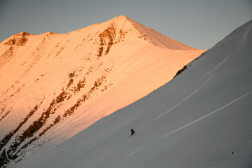 Fototapeta na wymiar Skier far away descends on slope of mountain at sunset