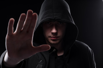 Fototapeta na wymiar A man in a black hood on a black background, studio photography. The idea of mysticism, mystery, crime and deception
