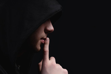 A man in a black hood on a black background, studio photography. The idea of mysticism, mystery,...
