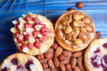 Mini tarts cupcakes with strawberries, nuts and blueberries on blue wooden background. Top view. Close up