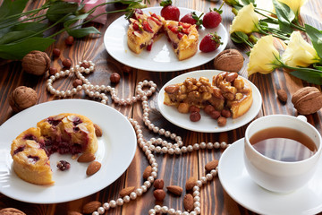 Fototapeta na wymiar Cup of coffee and three cut mini tarts cupcakes with strawberries, blueberries and with walnuts, almonds and hazelnuts on plate