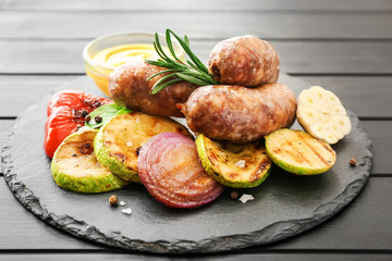 Slate plate with tasty grilled sausages, vegetables and sauce on table