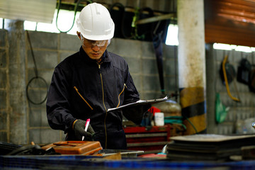 Engineer Industry holding tablet in hand of plan work with factory background , Engineer looking of working at industrial machinery setup in factory.