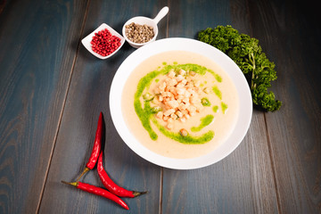 A plate of appetizing mushroom soup with croutons on a wooden table, among seasonings. Studio photography of food in the cooking industry, dark background.