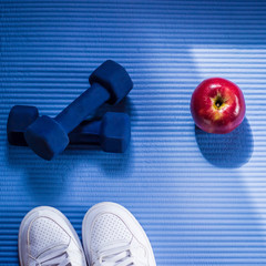 Dumbbells, apple and white gym shoes on the sport mat. Healthy lifestyle, fitness and sport.