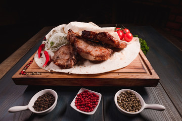 Appetizing fried meat lies on a wooden tray, among the seasonings. Studio photography of food in the cooking industry, dark background