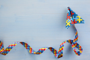 Autism awareness day or month. Paper plane in origami style with autism awareness puzzle ribbon on blue background.