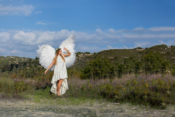 Beautiful woman in white angel outfit with wings in outdoor scenery