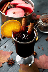 Mulled wine. Glass of winter hot drink with citrus, apple and spices. Stewpan  with mulled wine and cinnamon sticks, slice of oranges, anise and apple on wooden table.
