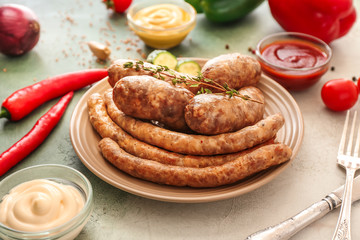 Plate with tasty grilled sausages and sauces on color background