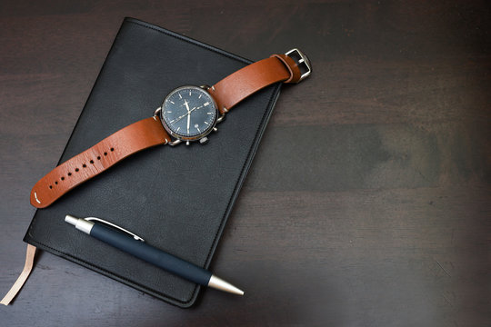 Top view of wristwatch on a notebook isolated on wooden table as background.  A prestige concept