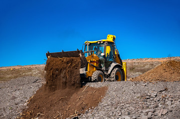 yellow bulldozer dumping rich soil for planting and dust control at waste pile