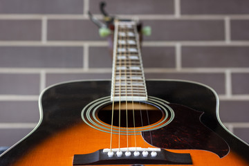 Fototapeta na wymiar Acoustic guitar closeup over brick wall background. Focus on sound hole and strings. Music industry, shallow depth of field, detail concepts