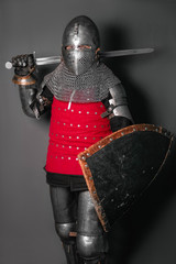 A medieval knight in armor with a shield and a sword in his hands stands in a fighting position and waves his weapon.