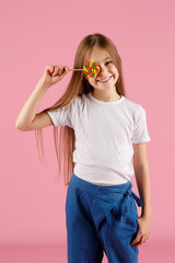 Portrait of a surprised little girl holding heart shaped lollipop and looking at camera isolated over pink background.