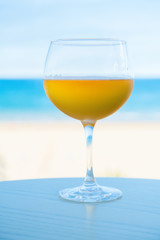 Glass of cider on the table against the beach. Cider with foam on the background of the blue sea.