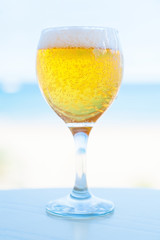 Glass of beer on the table against the beach, closeup. Beer with foam on the background of the sea.