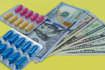 2 packages of colorful pills on the background of a pack of dollars