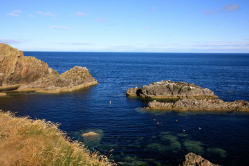 Fototapeta na wymiar Portknockie (Scotland), UK - August 01, 2018: Coastal landscape at Bow Fiddle Rock sea arch, Portknockie, Scotland, Highlands, United Kingdom