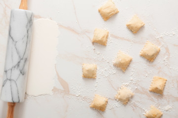 Raw ravioli with rolling pin on white background