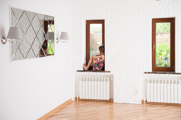 social distancing concept of thin little girl in dress sitting on window sill looking outside...