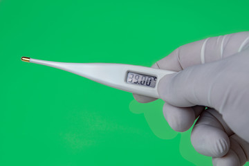Hand with a Thermometer on Green background. The thermometer shows a temperature of 39 Celsius. Coronavirus 2019-nCoV. Corona virus outbreaking.