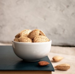 Inshell almonds in a white ceramic bowl on a light background with space for text.