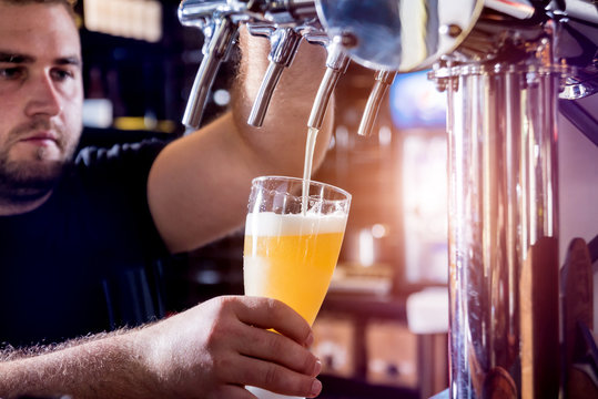 Bartender pouring draft beer at glasses in the bar. Restaurant.