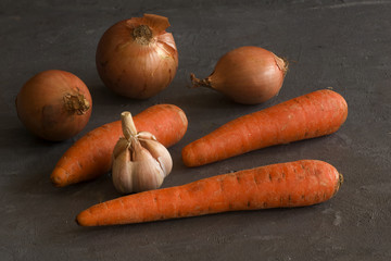 Some carrots, onions and garlic on a grey table