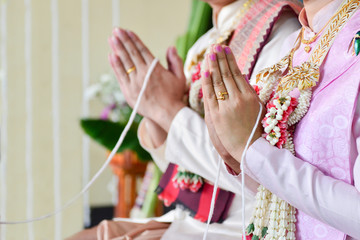 Obraz premium Bride and groom praying hand with holy thread blessing for happiness in their new family life.Thailand traditional wedding and engagement decoration accessories