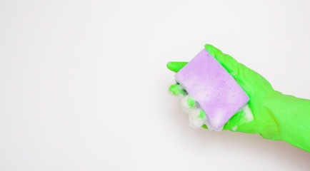 Hand in an green rubber glove with an purple sponge and foam on a white background. Washing dishes, cleaning, home cleaning.