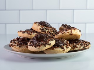 Plate piled high with thumbprint cookies with chocolate frosting and brown sprinkles, delicious, festive baked homemade baked goods, on a white counter with a white subway tile background.