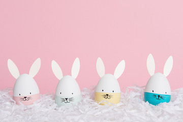 Easter eggs with bunny faces in nest on a pink background with space for copy