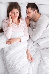 Young irritated woman in bed with snoring husband at home