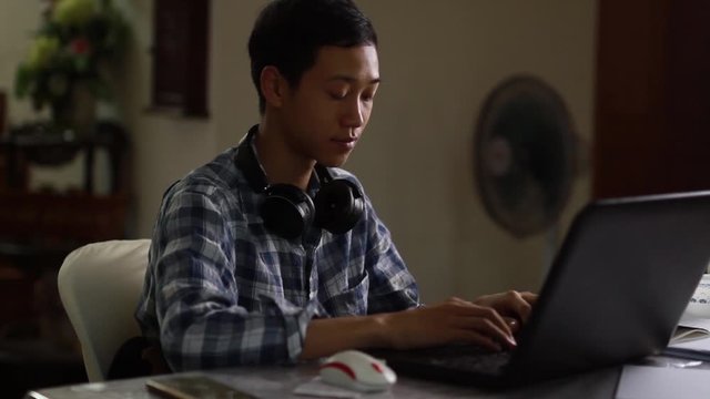 Teenager of Asian boy using an earphone for study on laptop at home. online class and home study concept.