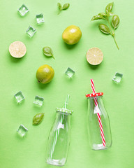 Fototapeta na wymiar Flat lay with ingredients for summer refreshing drink or smoothie, ice cubes, herbs and glass jars on green background, top view. Strawberry, lime, ice and basil for delicious summer cocktail