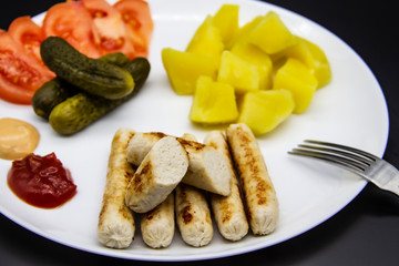 Delicious homemade chicken sausages with tomatoes, cucumbers, potato and souces. Fragrant sausages made from non-GMO chicken. Toasted Mini Sausages from chicken on the plate. Ukrainian tasty food.