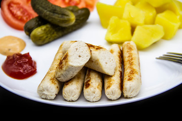 Delicious homemade chicken sausages with tomatoes, cucumbers, potato and souces. Fragrant sausages made from non-GMO chicken. Toasted Mini Sausages from chicken on the plate. Ukrainian tasty food.