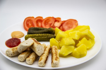 Delicious homemade chicken sausages with tomatoes, cucumbers, potato and souces. Fragrant sausages made from non-GMO chicken. Toasted Mini Sausages from chicken on the plate. Ukrainian tasty food.