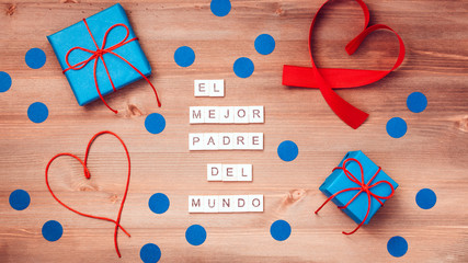 El mejor papa del mundo words that mean best dad in the world made of wooden blocks with blue gift boxes and red hearts on wooden background. Happy fathers day greeting card, top view - obrazy, fototapety, plakaty