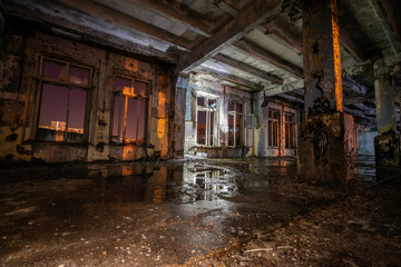 Fototapeta na wymiar Interior of an old abandoned soviet building with cracked ragged walls and leaking roof and wet floor at night with flashlights of stalkers