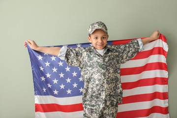 Little African-American soldier with USA flag on color background