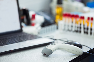 Bar codes scanner, blood sample tubes and laptop with lab technician hands on background. Coronavirus COVID-19 laboratory analysis workplace.