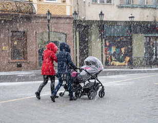 Family walking with the child in the stroller in snowy winter day.