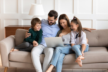 Happy couple cuddling kids siblings, watching comedy movie or funny cartoons on laptop together at...